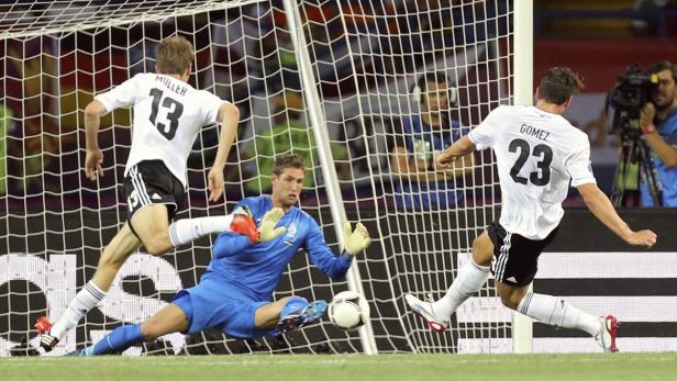 Mario Gomez schießt den Ball ins Tor, während Thomas Müller zusieht und der Torwart versucht, ihn abzuwehren.