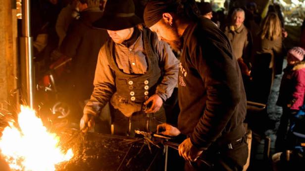 Zwei Schmiede arbeiten an einem Feuer auf einem Weihnachtsmarkt.