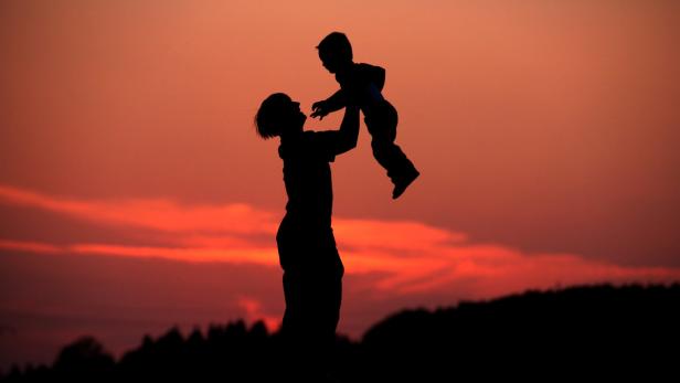 Die Silhouette einer Mutter, die ihr Kind in den Abendhimmel hebt.