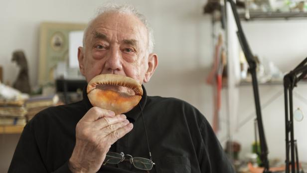 Ein älterer Mann hält eine große Kaurimuschel vor seinem Mund.