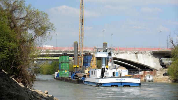 Ein Schiff namens „Magdalena“ mit einem Kran und Containern fährt auf einem Fluss unter einer beschädigten Brücke hindurch.