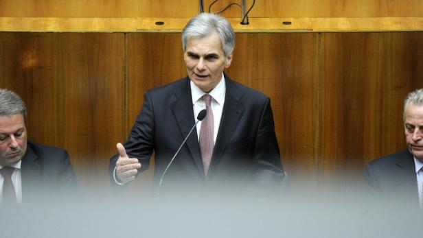 Ein Mann in einem Anzug spricht vor einem hölzernen Hintergrund.