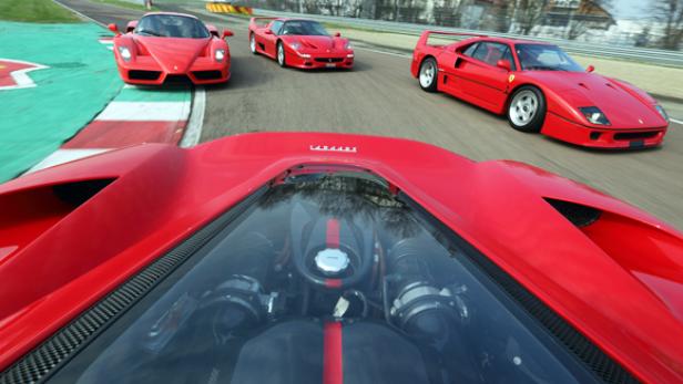 Ein roter Ferrari fährt auf einer Rennstrecke, gefolgt von drei weiteren roten Ferraris.
