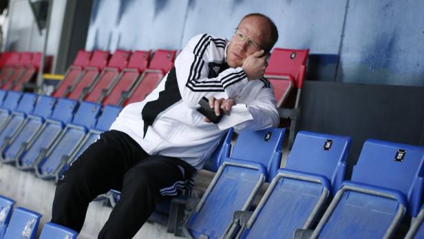 Ein Mann sitzt auf der Tribüne und telefoniert mit einem Handy am Ohr.