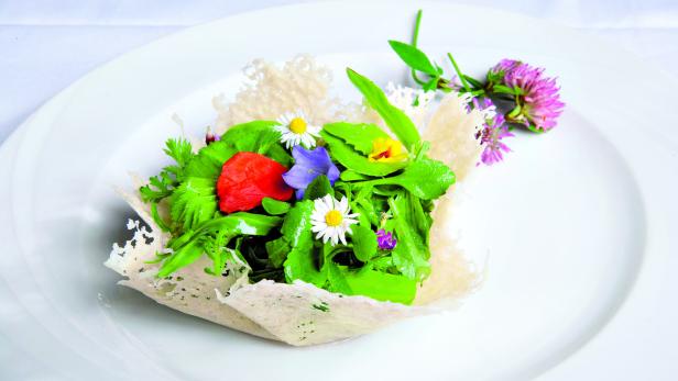 Ein Teller mit einem Salat aus verschiedenen grünen Blättern und bunten Blüten.
