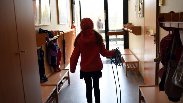 Ein Mädchen mit einer roten Jacke und Mütze geht einen Flur entlang.