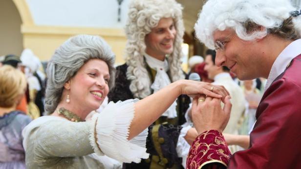 Eine Frau im historischen Kostüm berührt die Hand eines Mannes mit Perücke.