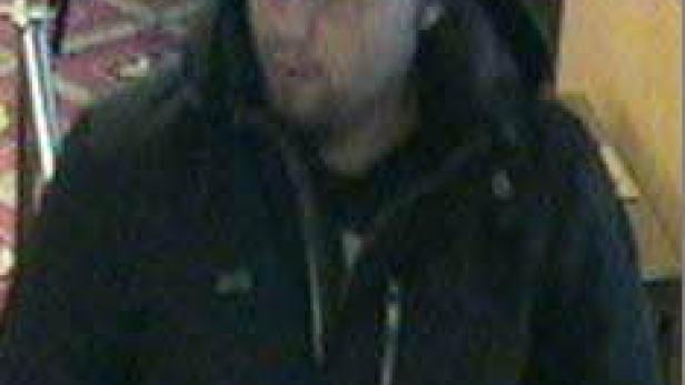 Ein Mann mit einer schwarzen Mütze und einer dunklen Jacke steht in einem Innenraum.