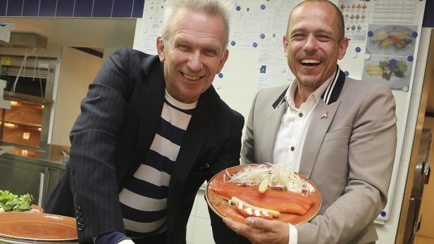 Zwei Männer präsentieren lachend einen Teller mit Lachs und Spargel in einer Küche.