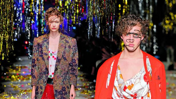 Zwei Models präsentieren Mode auf einem Laufsteg mit glitzerndem Hintergrund.