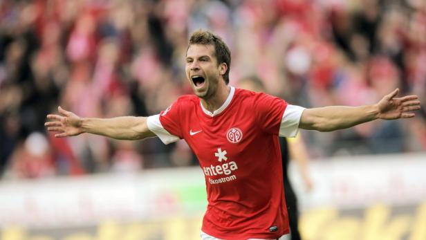 Ein Fußballspieler im roten Trikot jubelt mit ausgestreckten Armen.