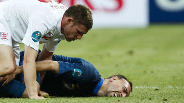 Ein englischer Fußballspieler steht über einem am Boden liegenden französischen Spieler.