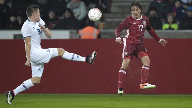 Ein Fußballspieler aus Island schießt den Ball, während ein dänischer Spieler zusieht.