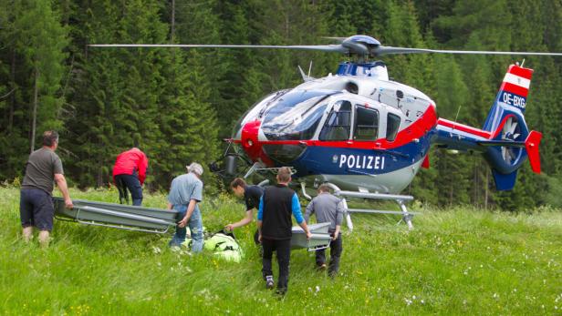 Ein Team transportiert eine Trage zu einem Polizei-Hubschrauber auf einer Wiese.