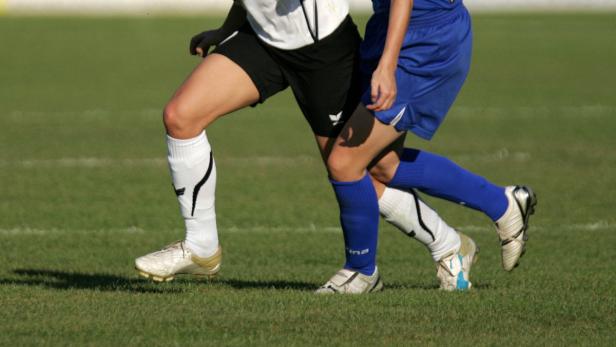 Zwei Fußballspielerinnen im Zweikampf auf einem grünen Rasen.