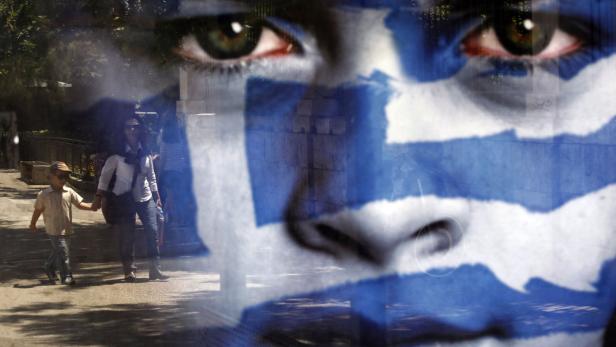 Eine Frau und ein Kind gehen an einem Schaufenster mit der griechischen Flagge vorbei.