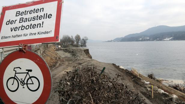 Ein Baustellenschild und ein Fahrradverbotsschild stehen an einem Uferweg am See.