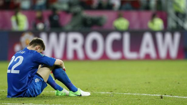 Ein Fußballspieler sitzt enttäuscht auf dem Rasen vor einer Werbetafel mit der Aufschrift „Wroclaw“.