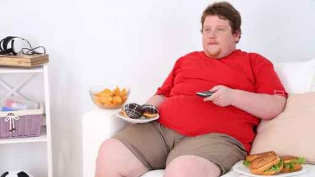 Ein Mann sitzt mit Snacks und Fernbedienung auf dem Sofa.