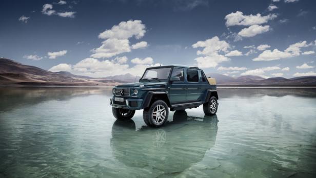Ein türkisfarbener Mercedes-Benz G 650 Landaulet steht im flachen Wasser vor einer Bergkulisse.