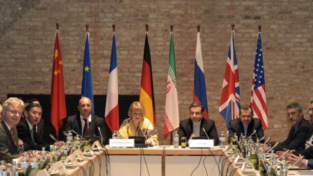 Delegierte sitzen an einem Tisch vor den Flaggen verschiedener Nationen bei einer internationalen Konferenz.