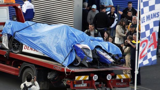 Ein beschädigtes Rennauto, teilweise mit einer blauen Plane bedeckt, wird auf einem Abschleppwagen transportiert.