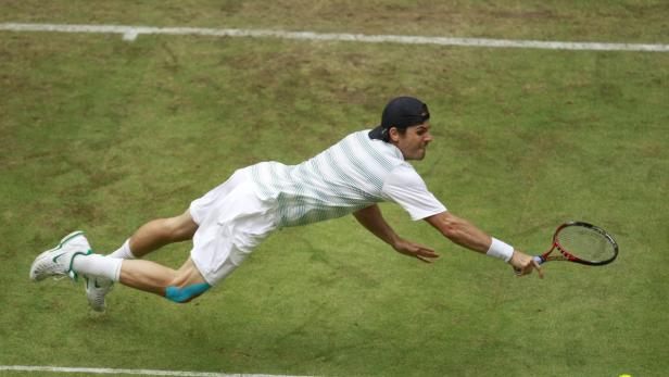 Ein Tennisspieler hechtet über einen Rasenplatz, um einen Ball zu erreichen.