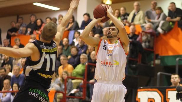 Ein Basketballspieler wirft den Ball, während ein Gegenspieler ihn zu blocken versucht.