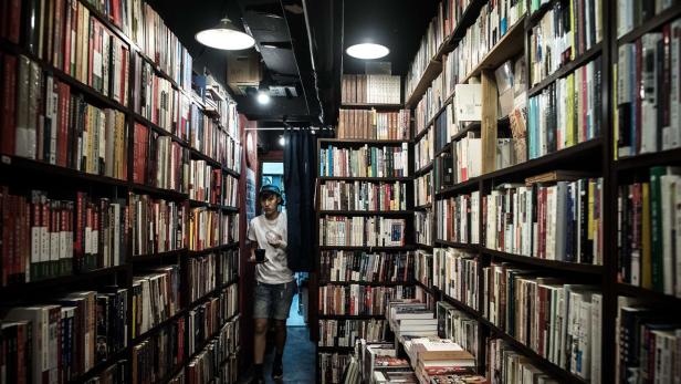 Ein Mann geht durch einen schmalen Gang, der von Bücherregalen gesäumt ist.