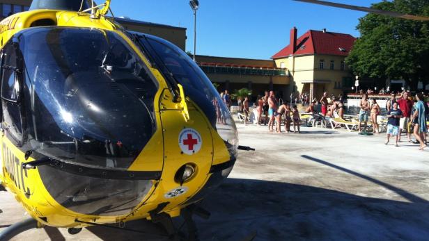 Ein gelber Rettungshubschrauber des Österreichischen Roten Kreuzes steht vor einem Schwimmbad.