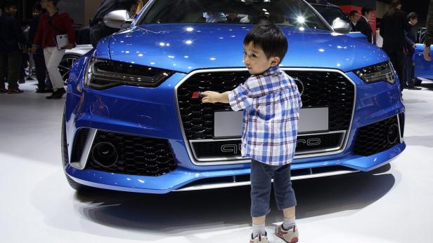 Ein kleiner Junge berührt das Logo eines blauen Audi RS6 auf einer Automobilausstellung.
