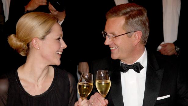 Eine Frau und ein Mann im Smoking stoßen mit Weißwein an.
