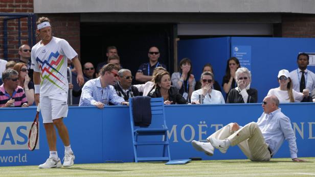 Ein Tennisspieler steht auf dem Platz, während ein Zuschauer im Publikum hinfällt.