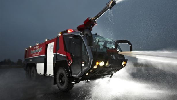 Ein rotes Flughafenlöschfahrzeug sprüht Wasser aus mehreren Düsen.