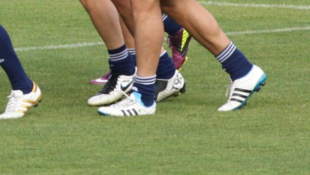 Mehrere Fußballspieler mit Stutzen und Fußballschuhen auf einem Rasenplatz.