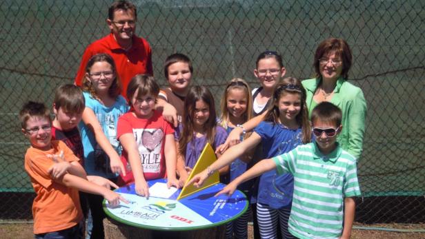 Eine Gruppe Kinder und zwei Erwachsene stehen um eine Drehscheibe mit dem Logo von Limbach und OBI.