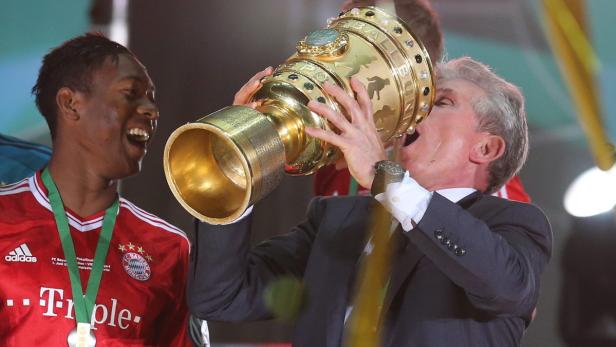 Uli Hoeneß trinkt aus dem DFB-Pokal, während David Alaba danebensteht und lacht.