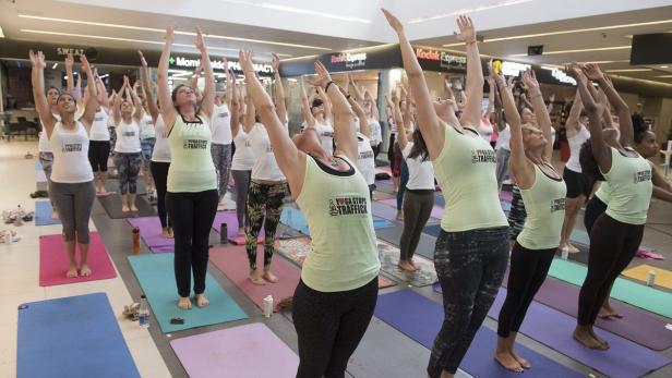 Eine Gruppe von Frauen praktiziert Yoga mit erhobenen Armen in einem Einkaufszentrum.