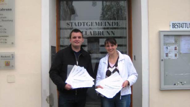 Ein Mann und eine Frau stehen vor der Stadtgemeinde Ebreichsdorf und halten Papiere in den Händen.