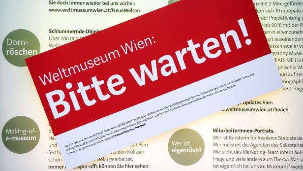 Ein rotes Schild wirbt für das Weltmuseum Wien: „Bitte warten!“.