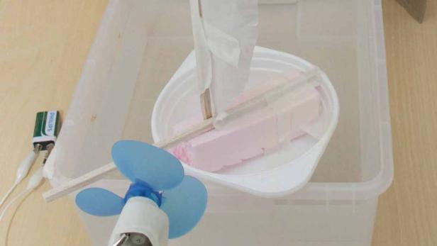 Ein selbstgebautes Spielzeugboot mit Ventilator in einem Wasserbecken.