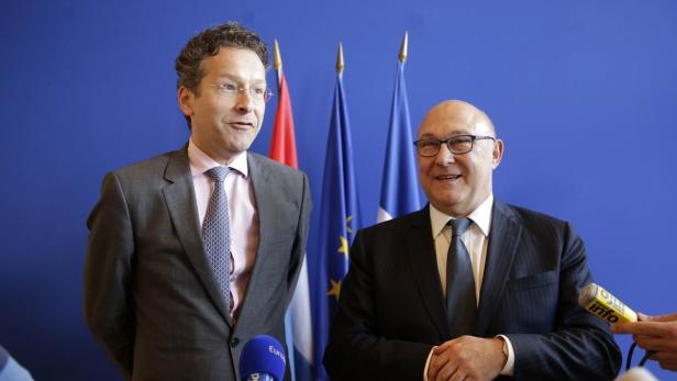 Zwei Männer in Anzügen stehen vor Flaggen.