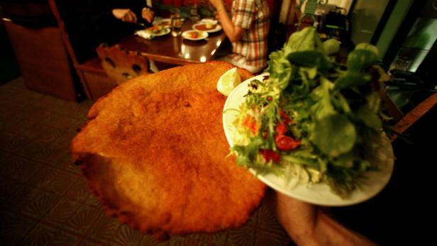 Ein riesiges Schnitzel mit einem Zitronenschnitz und einem Salat wird serviert.