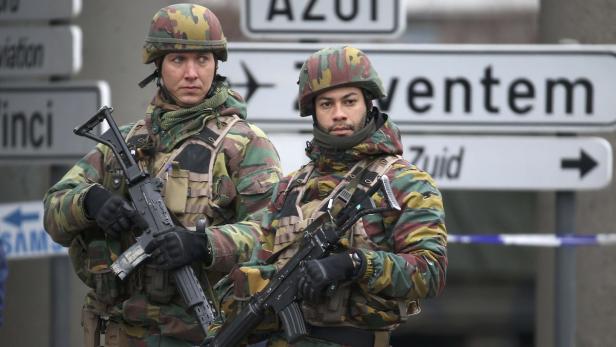 Zwei belgische Soldaten mit Gewehren stehen vor Wegweisern in Zaventem.
