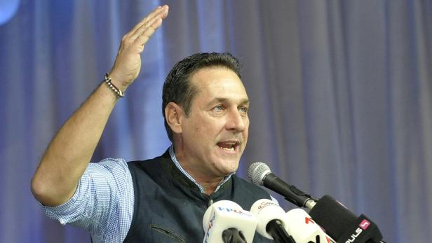 Ein Mann gestikuliert bei einer Rede vor Mikrofonen.