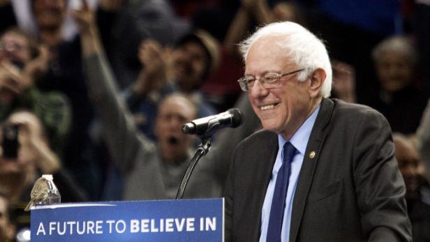 Bernie Sanders lächelt bei einer Rede vor einer jubelnden Menschenmenge.
