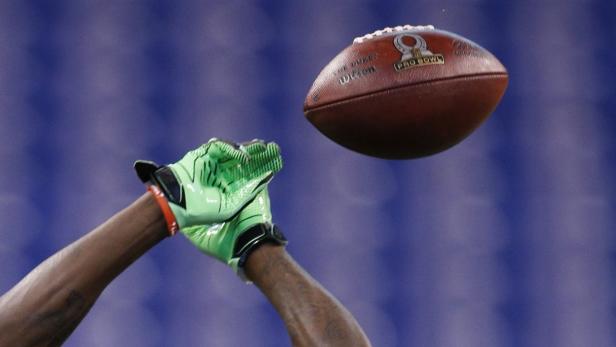 Ein Football schwebt über den Händen eines Spielers mit grünen Handschuhen.