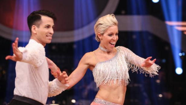 Ein Tanzpaar in glitzernden Kostümen tanzt auf einer Bühne.