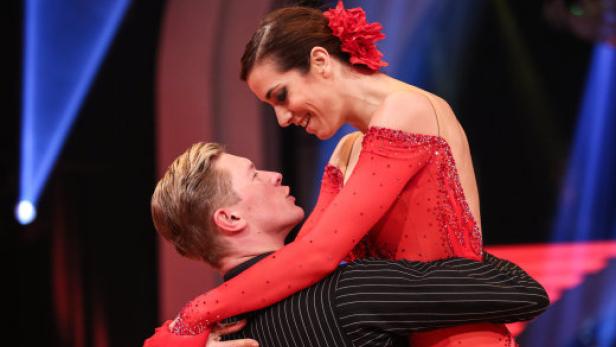 Ein Tanzpaar in roter und gestreifter Kleidung blickt sich an.