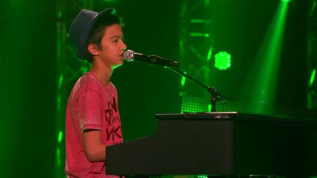 Ein junger Sänger mit Hut performt am Klavier vor grünem Bühnenlicht.